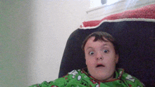 a young boy with a surprised look on his face is wearing a green pajama top