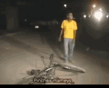 a man in a yellow shirt walks past a bicycle that has been knocked over and says pinches mameys