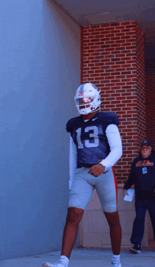a football player with the number 13 on his jersey stands in front of a brick wall