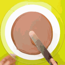 a person spreading chocolate frosting on a cake with a spatula