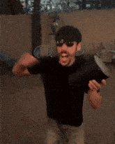 a man wearing sunglasses and a black shirt is holding a black object that looks like a flamethrower