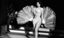 a black and white photo of a woman in a feathered costume holding a fan .