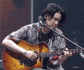 a man is playing a guitar in front of a microphone .