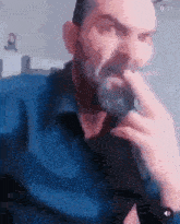 a man with a beard is sitting on a couch and holding his hand to his mouth .