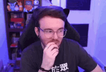 a man with glasses and a beard is sitting in a chair with his hand on his chin .