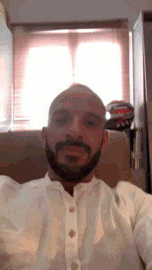 a bald man with a beard is sitting in a chair in front of a window