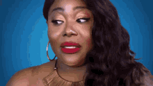 a woman with red lipstick and gold earrings is making a funny face against a blue background .