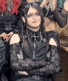 a woman with long black hair and glasses is sitting with her arms crossed and looking at the camera .