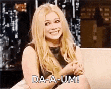 a woman is sitting on a couch and smiling while holding her hands together .