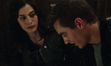 a man and a woman are looking at each other and the man is wearing a leather jacket