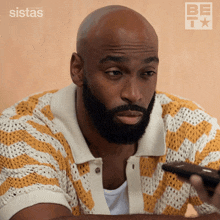 a bald man with a beard is holding a remote control in front of a sistas logo