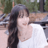 a young woman wearing a white top and necklace smiles