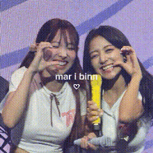 two women are making a heart shape with their hands while holding a microphone .
