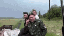 a man in a military uniform is talking on a cell phone with two other men .
