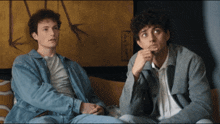 two young men are sitting on a couch and one has his hand on his chin