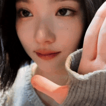 a close up of a woman 's face with her hand making a heart shape