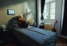 a gif from gifrun.com shows a woman sitting on a bed in a bedroom