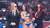 a woman in a blue and gold outfit is standing in a wrestling ring with two other women