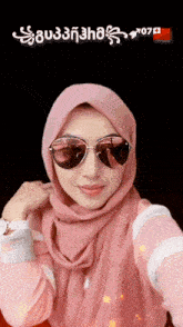 a woman wearing a pink hijab and sunglasses takes a picture