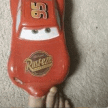 a person is holding a toy lightning mcqueen car with their foot .