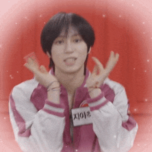 a young man wearing a pink and white jacket is making a heart with his hands .