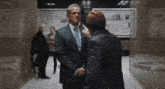 a man in a suit and tie talking to another man in a hallway