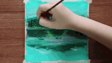 a person is painting a landscape with a brush on a piece of paper