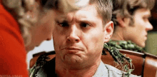 a man is making a funny face while sitting in a chair with a woman standing behind him .