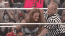 a referee is holding a woman in a wrestling ring while a crowd watches