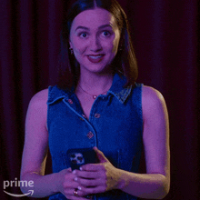 a woman in a blue denim vest is holding a cell phone in front of a prime logo
