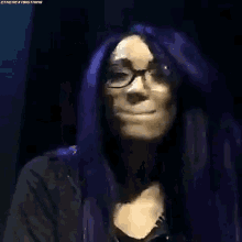 a woman with purple hair and glasses is smiling and making a face .