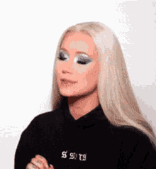 a woman with blonde hair and blue eyeshadow is wearing a black hoodie and making a funny face .