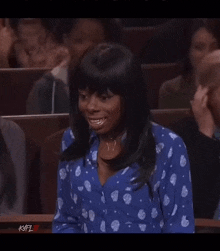 a woman in a blue polka dot shirt is sitting in a courtroom .