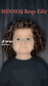 a little girl with curly hair is wearing a black shirt and smiling for the camera