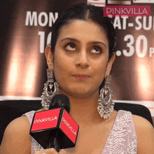 a woman wearing earrings holds a pinkvilla microphone in her hand