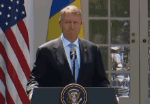 a man in a suit and tie stands at a podium with the united states of america seal on it
