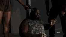 a man in a camo tank top is wrapped in bandages and a bet advertisement is behind him