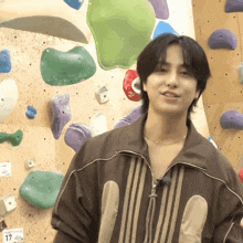 a young man stands in front of a climbing wall with a number 17 on it