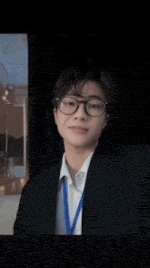 a young man wearing glasses and a suit is sitting in front of a blue curtain .
