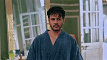 a man wearing a blue robe is standing in front of a mirror .