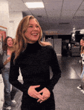 a woman wearing a black turtleneck is laughing in a hallway
