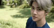 a young man with gray hair is wearing a blue shirt and standing in a field .