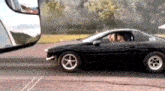 a black car is driving down a road next to a rear view mirror .
