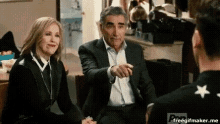 a man in a suit and tie is sitting next to a woman and a man in a black shirt .