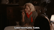 a woman is sitting at a table smoking a cigarette and saying land this plane carol
