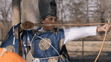 a man in a blue and gold kimono is aiming a bow and arrow