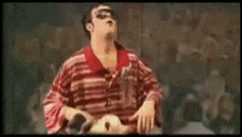 a man in a red and white striped shirt is holding a goat .