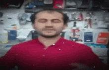 a man in a red shirt is standing in a store with his eyes closed and a beard .