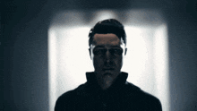 a man in a black jacket is standing in a dark room looking at the camera