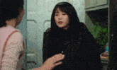 a woman in a brown jacket is talking to another woman in a pink shirt